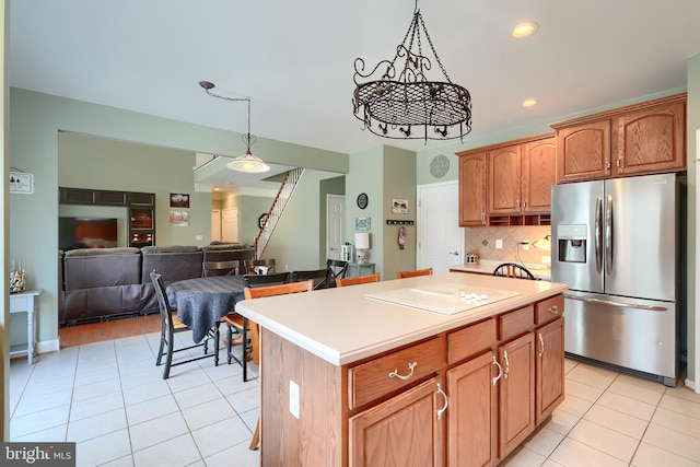 kitchen with decorative light fixtures, a center island, light tile patterned floors, stainless steel fridge, and backsplash