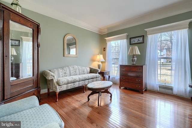 living area with crown molding, a wealth of natural light, and light hardwood / wood-style floors