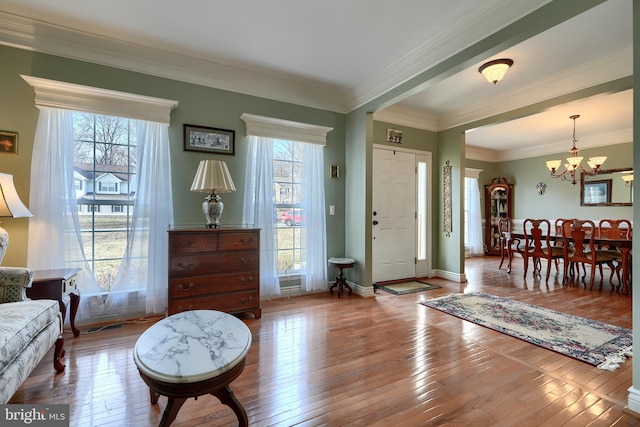 foyer entrance featuring wood-type flooring, ornamental molding, and a notable chandelier