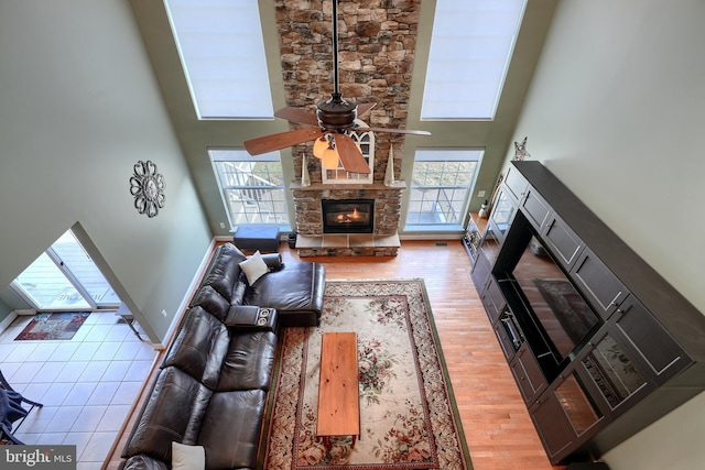 living room with a high ceiling, ceiling fan, a fireplace, and light hardwood / wood-style floors