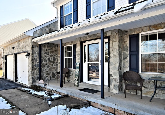 snow covered property entrance with a porch and a garage