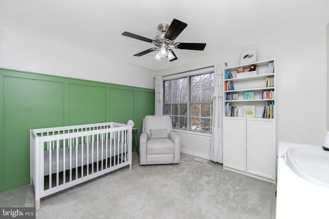 bedroom featuring ceiling fan, light carpet, and a crib