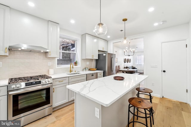 kitchen with sink, a kitchen island, light stone countertops, and appliances with stainless steel finishes