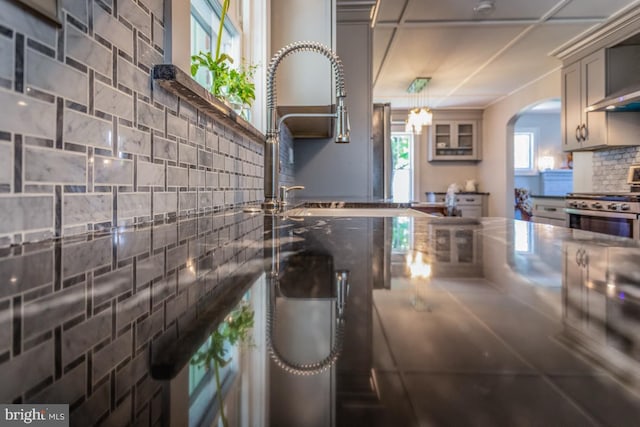 room details featuring stainless steel stove, tasteful backsplash, sink, hanging light fixtures, and wall chimney exhaust hood