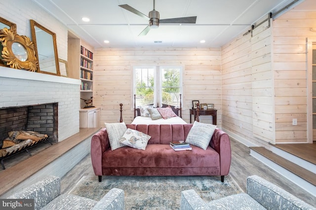 bedroom featuring a barn door, hardwood / wood-style floors, wooden walls, and a brick fireplace