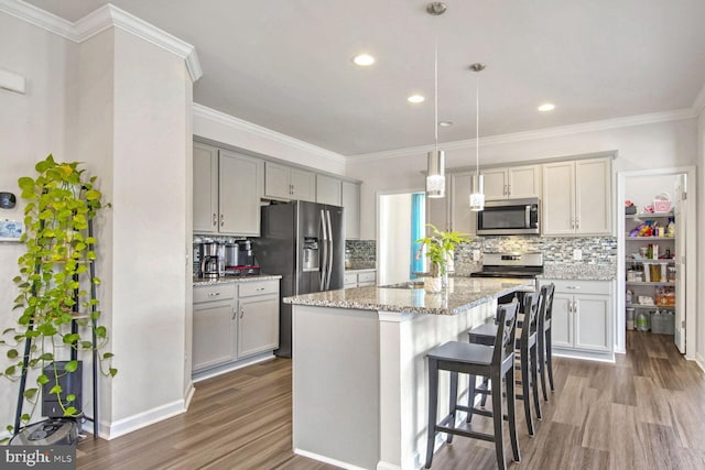 kitchen with appliances with stainless steel finishes, an island with sink, gray cabinetry, hanging light fixtures, and hardwood / wood-style flooring