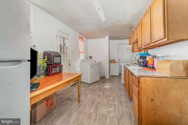 kitchen with washer and dryer, light countertops, freestanding refrigerator, and a sink