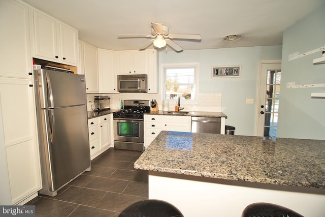 kitchen with stainless steel appliances, sink, white cabinets, and dark stone counters