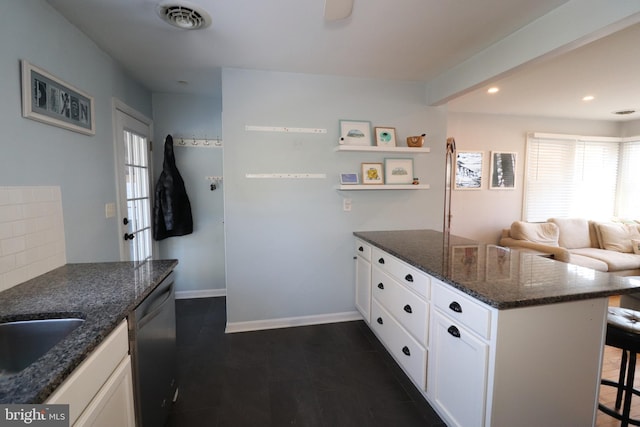 kitchen featuring a breakfast bar area, dishwasher, white cabinets, dark stone counters, and backsplash