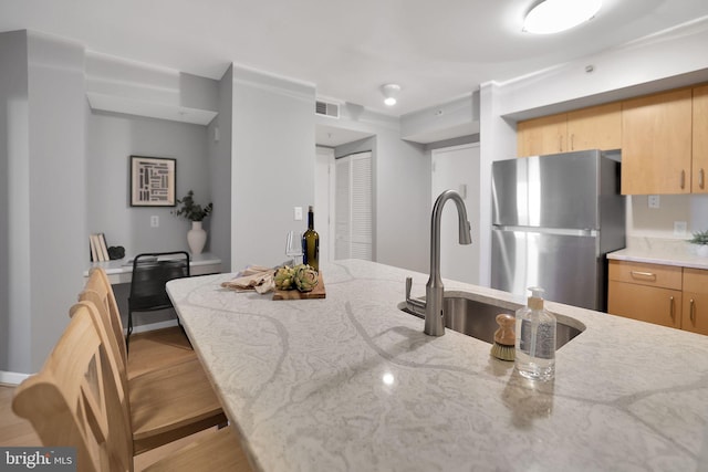 kitchen with light brown cabinetry, light stone counters, light hardwood / wood-style flooring, stainless steel fridge, and a kitchen breakfast bar