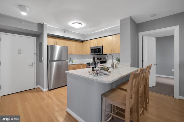 kitchen featuring a kitchen breakfast bar, stainless steel appliances, light hardwood / wood-style floors, light brown cabinetry, and kitchen peninsula