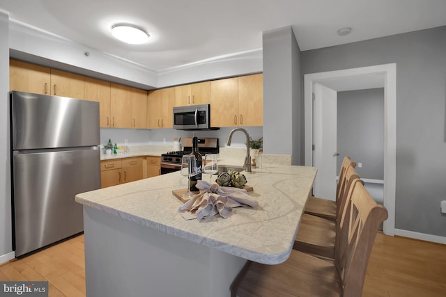 kitchen featuring appliances with stainless steel finishes, light brown cabinetry, light hardwood / wood-style floors, and kitchen peninsula