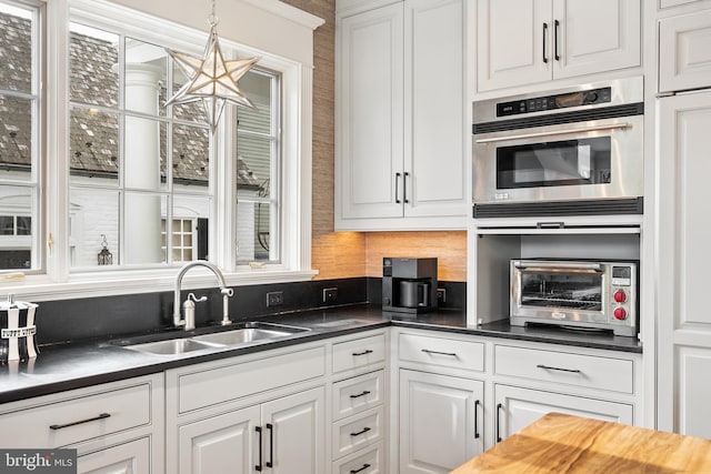 kitchen featuring hanging light fixtures, sink, stainless steel double oven, and white cabinets