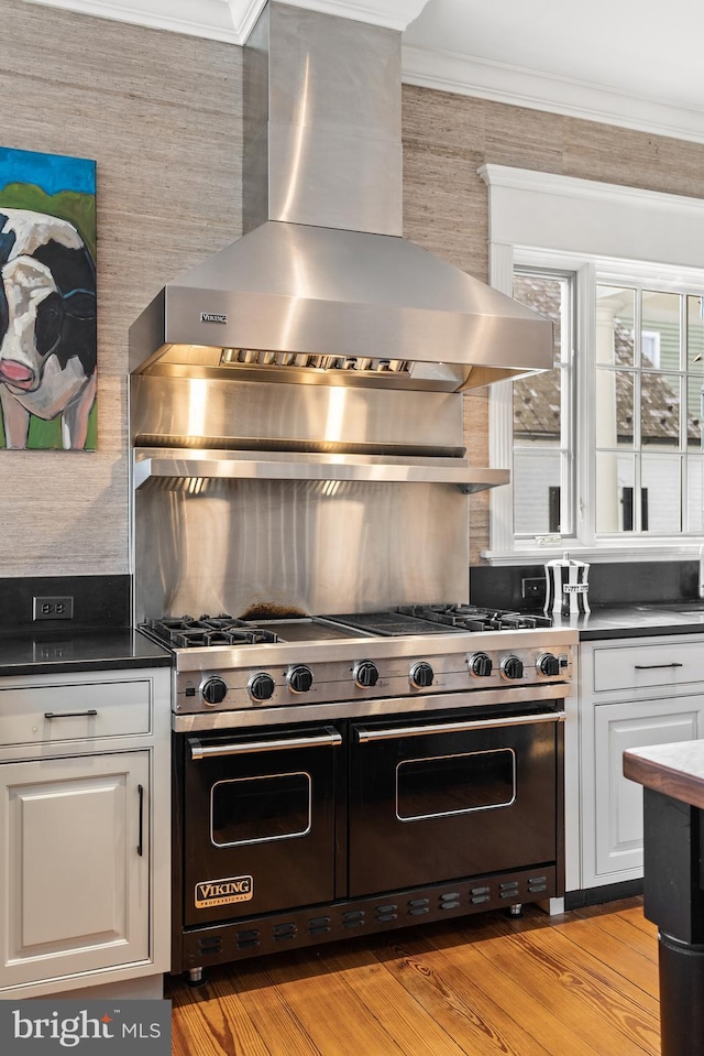 kitchen with white cabinetry, double oven range, light hardwood / wood-style floors, crown molding, and wall chimney range hood