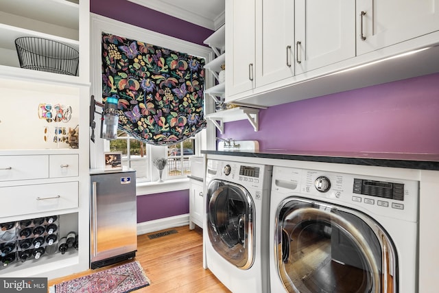 clothes washing area featuring separate washer and dryer, light hardwood / wood-style flooring, ornamental molding, and cabinets