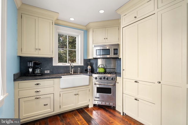 kitchen with tasteful backsplash, sink, stainless steel appliances, cream cabinets, and dark wood-type flooring