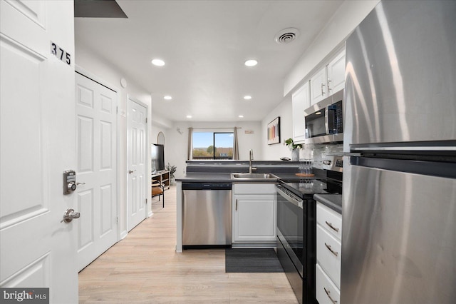 kitchen featuring appliances with stainless steel finishes, sink, white cabinets, kitchen peninsula, and light hardwood / wood-style flooring