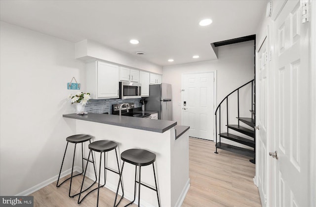 kitchen with light hardwood / wood-style flooring, appliances with stainless steel finishes, backsplash, white cabinets, and kitchen peninsula