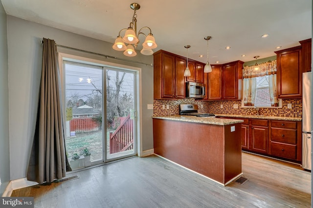 kitchen with stainless steel appliances, light stone countertops, decorative backsplash, decorative light fixtures, and kitchen peninsula