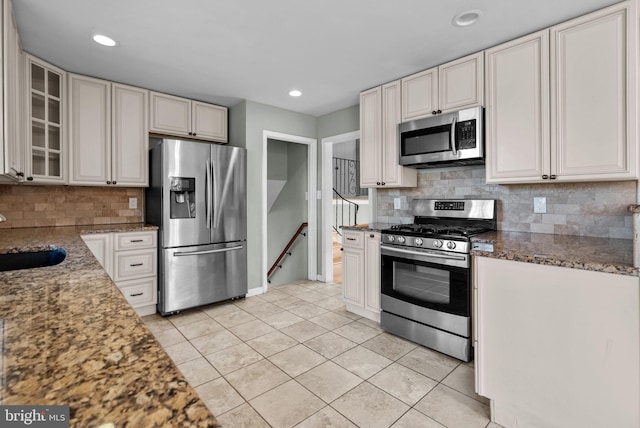 kitchen with sink, light tile patterned floors, appliances with stainless steel finishes, dark stone countertops, and white cabinetry