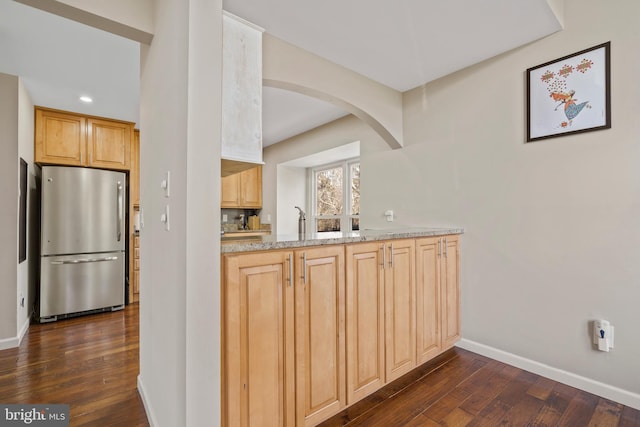 kitchen featuring dark wood-type flooring, light stone counters, stainless steel fridge, and light brown cabinetry