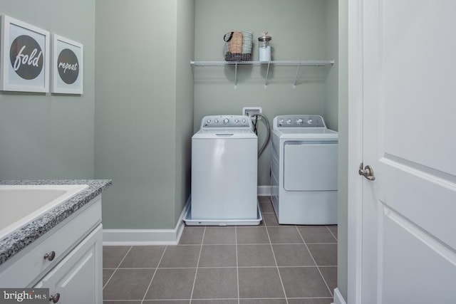 clothes washing area featuring dark tile patterned floors, sink, washing machine and clothes dryer, and cabinets