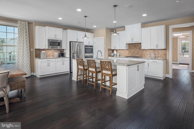 kitchen with white cabinetry, hanging light fixtures, a center island with sink, and appliances with stainless steel finishes