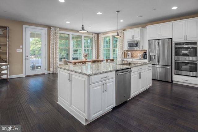 kitchen with appliances with stainless steel finishes, white cabinetry, sink, hanging light fixtures, and a center island with sink