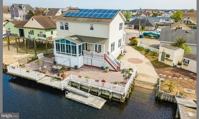 rear view of house featuring a sunroom, solar panels, and a water view