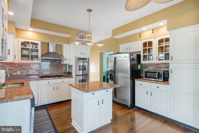 kitchen featuring sink, decorative light fixtures, appliances with stainless steel finishes, wall chimney range hood, and white cabinets