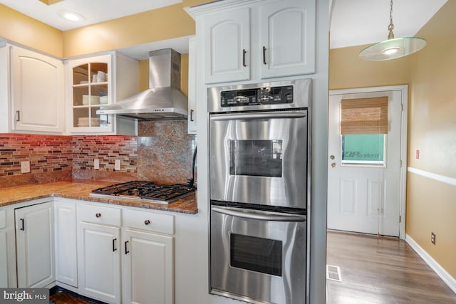 kitchen featuring wall chimney range hood, decorative light fixtures, white cabinets, and appliances with stainless steel finishes