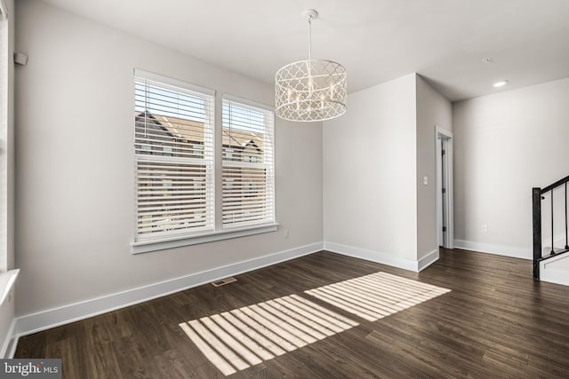 unfurnished dining area featuring dark wood-type flooring and an inviting chandelier