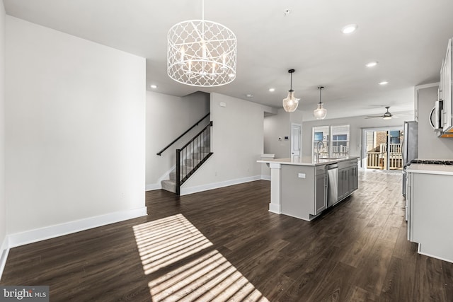 kitchen featuring dark wood-type flooring, sink, decorative light fixtures, stainless steel appliances, and a kitchen island with sink