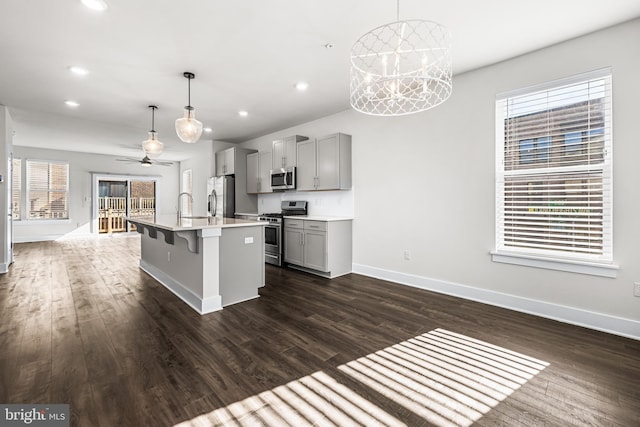 kitchen with stainless steel appliances, pendant lighting, gray cabinetry, and a center island with sink