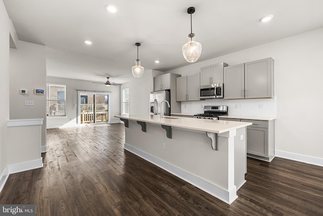 kitchen with hanging light fixtures, appliances with stainless steel finishes, gray cabinets, an island with sink, and decorative backsplash