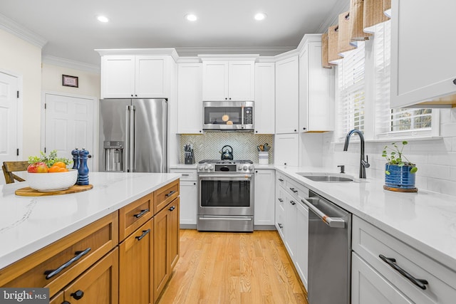 kitchen with stainless steel appliances, light stone countertops, sink, and white cabinets