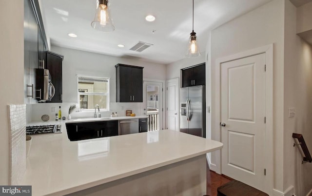 kitchen with appliances with stainless steel finishes, light countertops, decorative light fixtures, and a peninsula