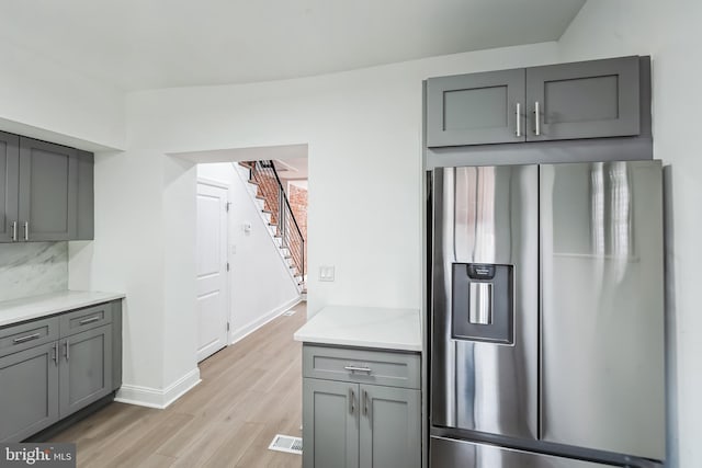 kitchen featuring gray cabinets, light hardwood / wood-style flooring, decorative backsplash, and stainless steel fridge with ice dispenser