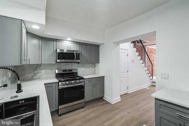 kitchen featuring stainless steel appliances, gray cabinets, backsplash, and light hardwood / wood-style floors