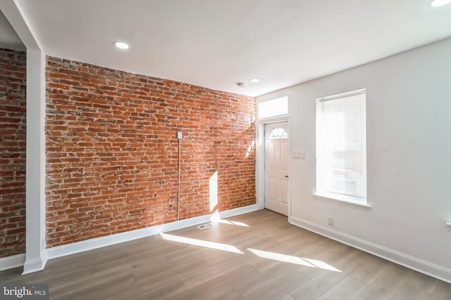 unfurnished room with brick wall and light hardwood / wood-style flooring