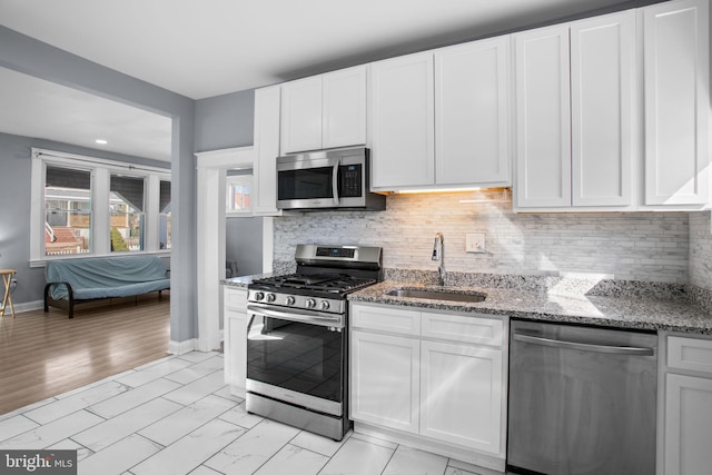 kitchen with light stone countertops, a sink, decorative backsplash, stainless steel appliances, and white cabinetry