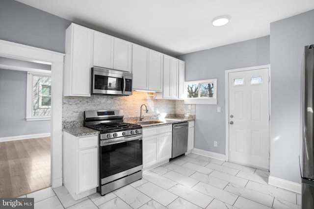 kitchen featuring marble finish floor, a sink, tasteful backsplash, appliances with stainless steel finishes, and light stone countertops