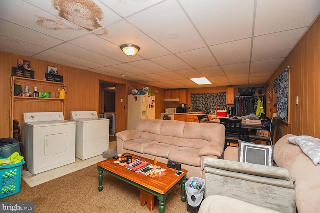 living room featuring independent washer and dryer, light tile patterned floors, wood walls, and a drop ceiling