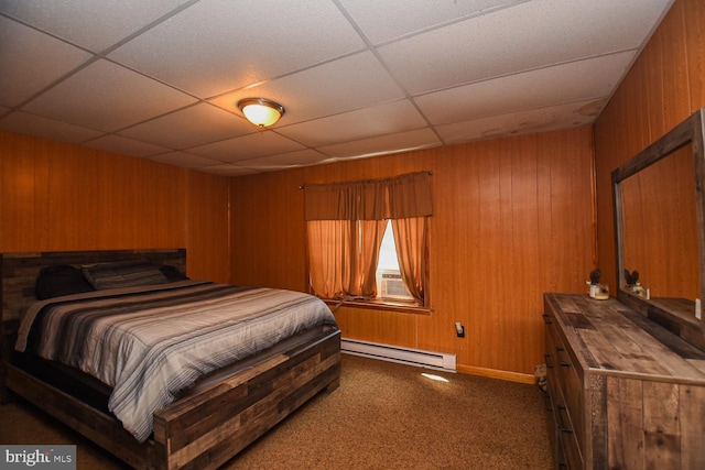 bedroom featuring a paneled ceiling, wooden walls, dark carpet, and a baseboard heating unit