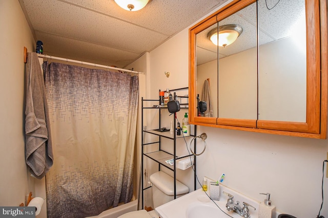 full bathroom with shower / bath combo, sink, a drop ceiling, and toilet