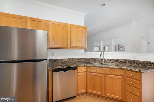 kitchen featuring sink, crown molding, light hardwood / wood-style flooring, dark stone countertops, and stainless steel appliances