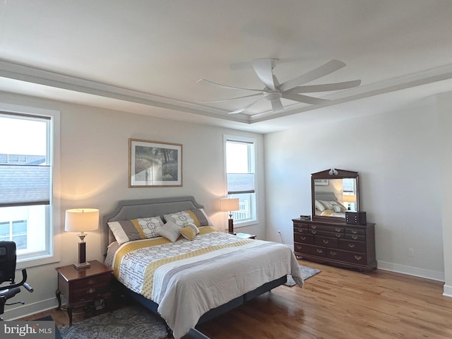 bedroom featuring multiple windows, a tray ceiling, light hardwood / wood-style floors, and ceiling fan