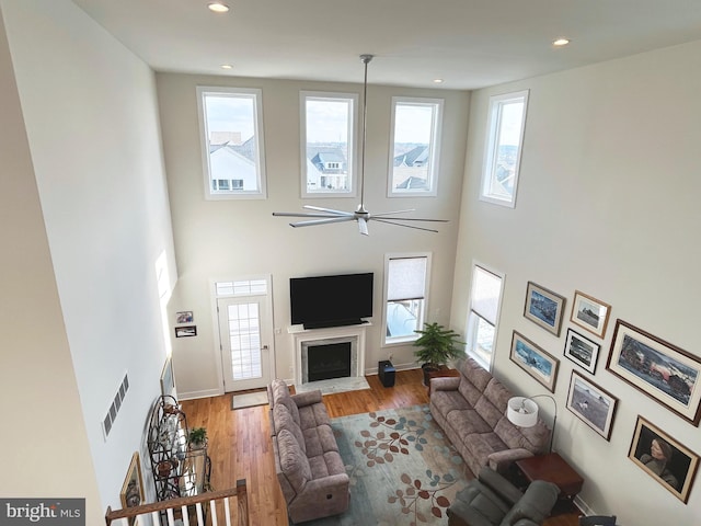 living room featuring a towering ceiling, wood-type flooring, and ceiling fan