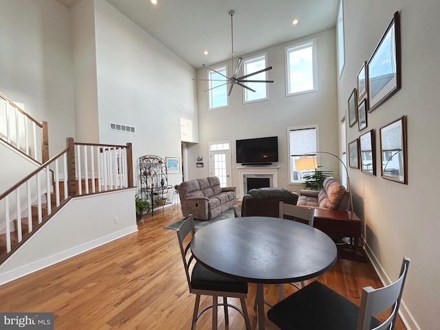 dining room with a high ceiling, ceiling fan, a wealth of natural light, and light hardwood / wood-style floors