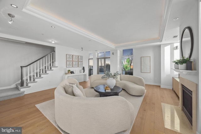 living room featuring a high end fireplace, light hardwood / wood-style floors, and a tray ceiling